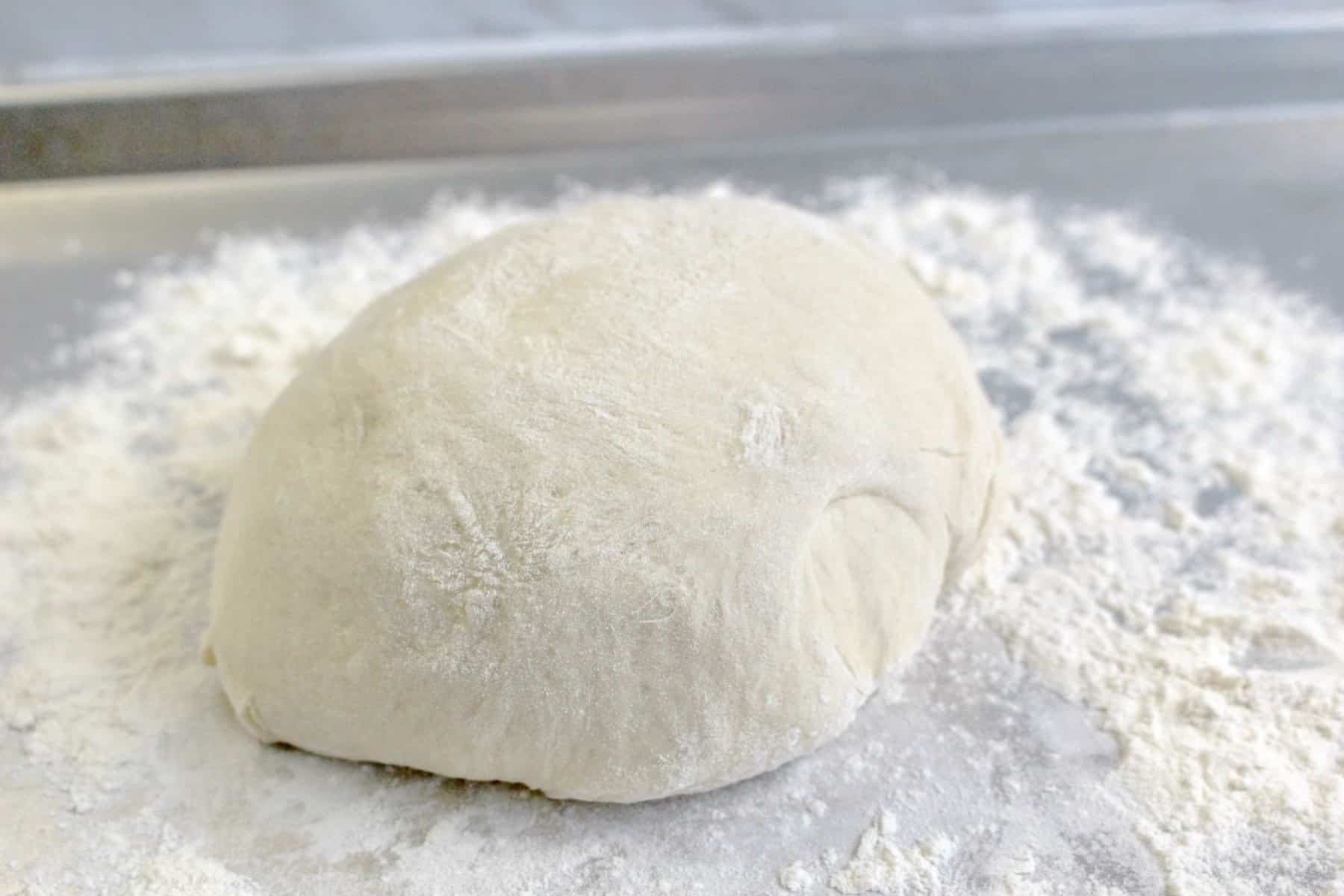 Pizza dough ball resting on a floured work surface.