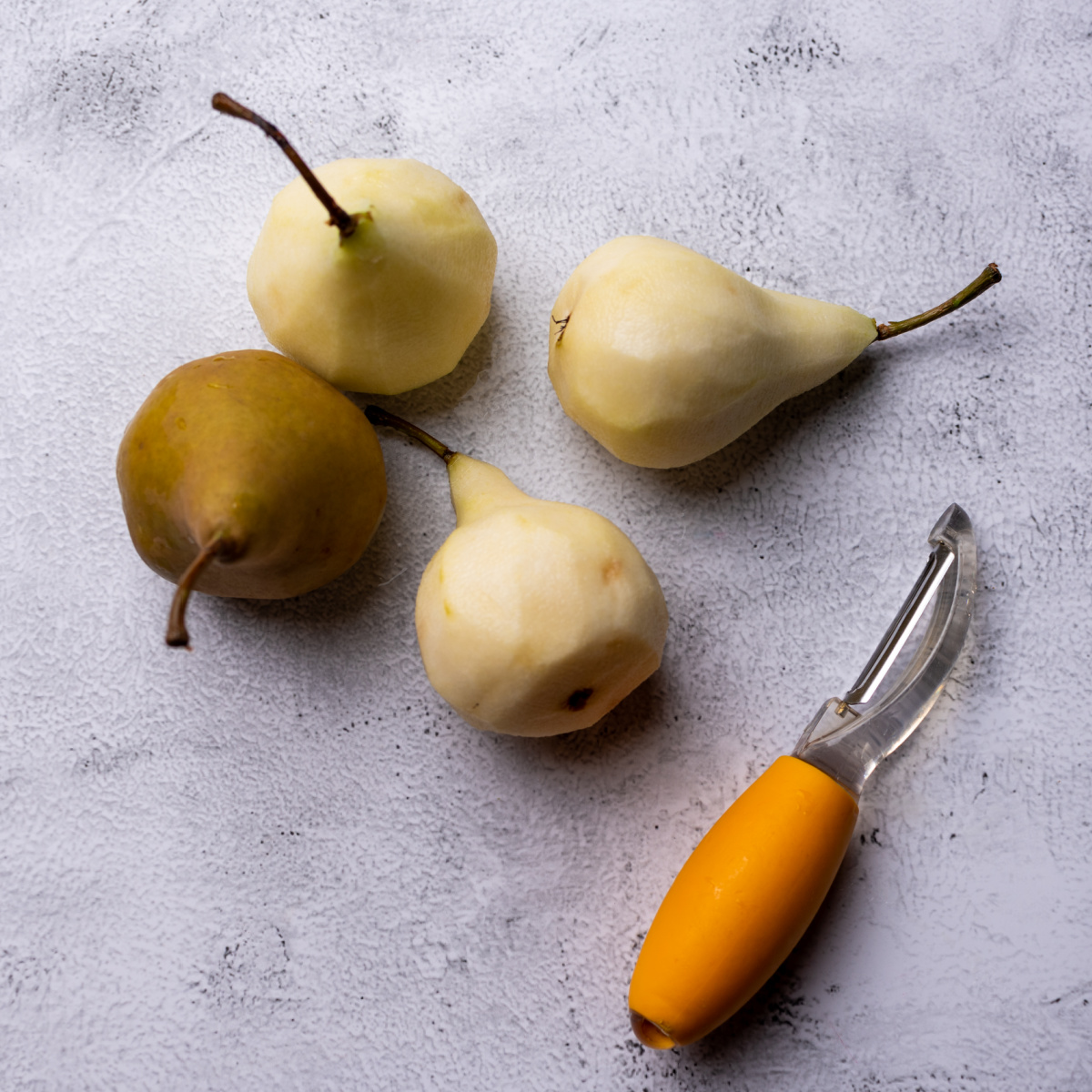 3 peeled pears and 1 with the skin still on and a peeler.