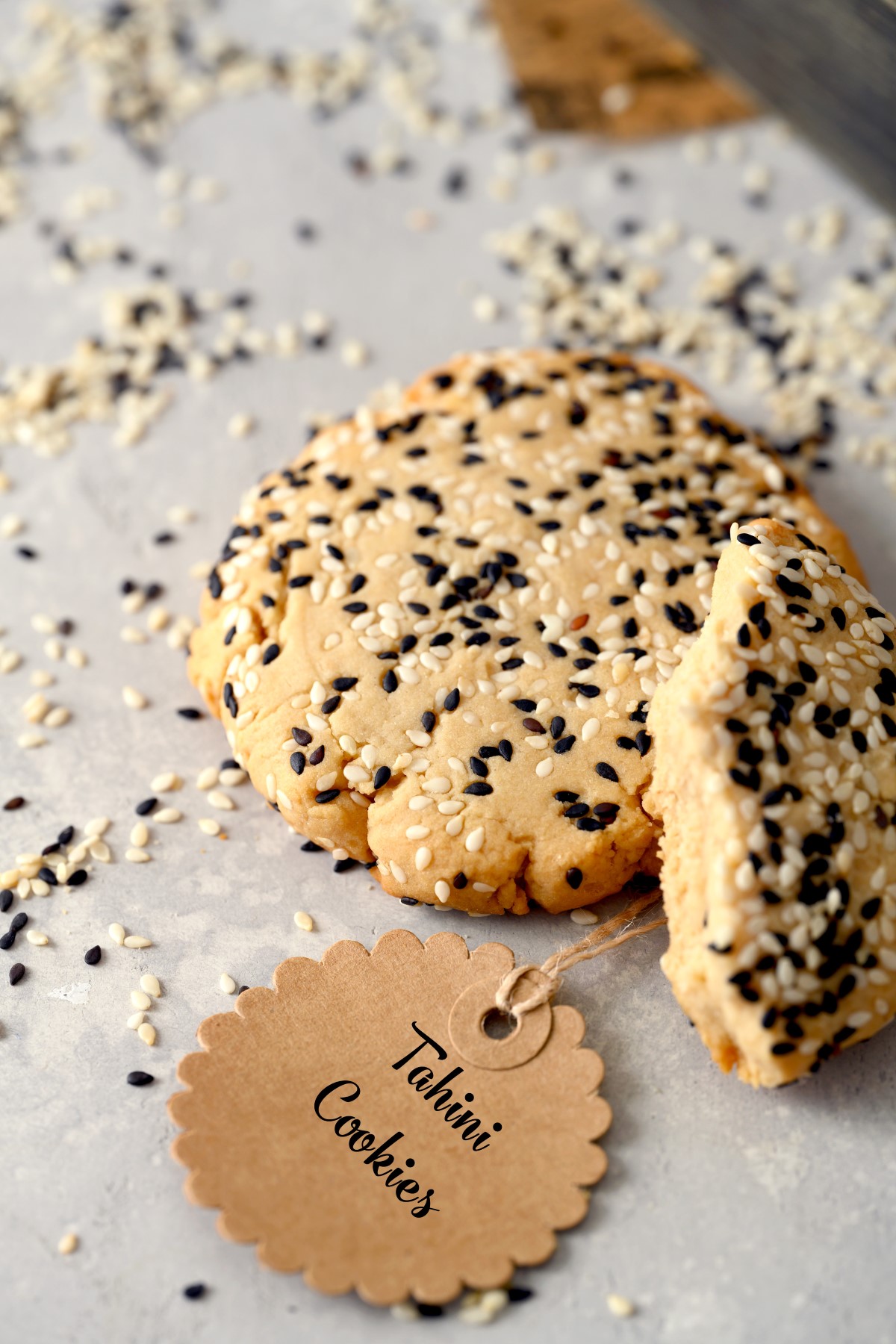 A broken tahini cookie with a whole one and a tag reading tahini cookies. 