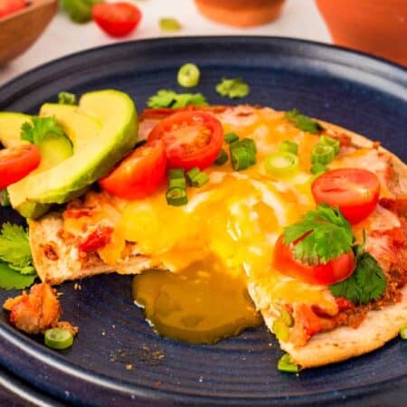 Showing a runny egg yolk coming off of a Sheet Pan Huevos Rancheros on a blue plate.