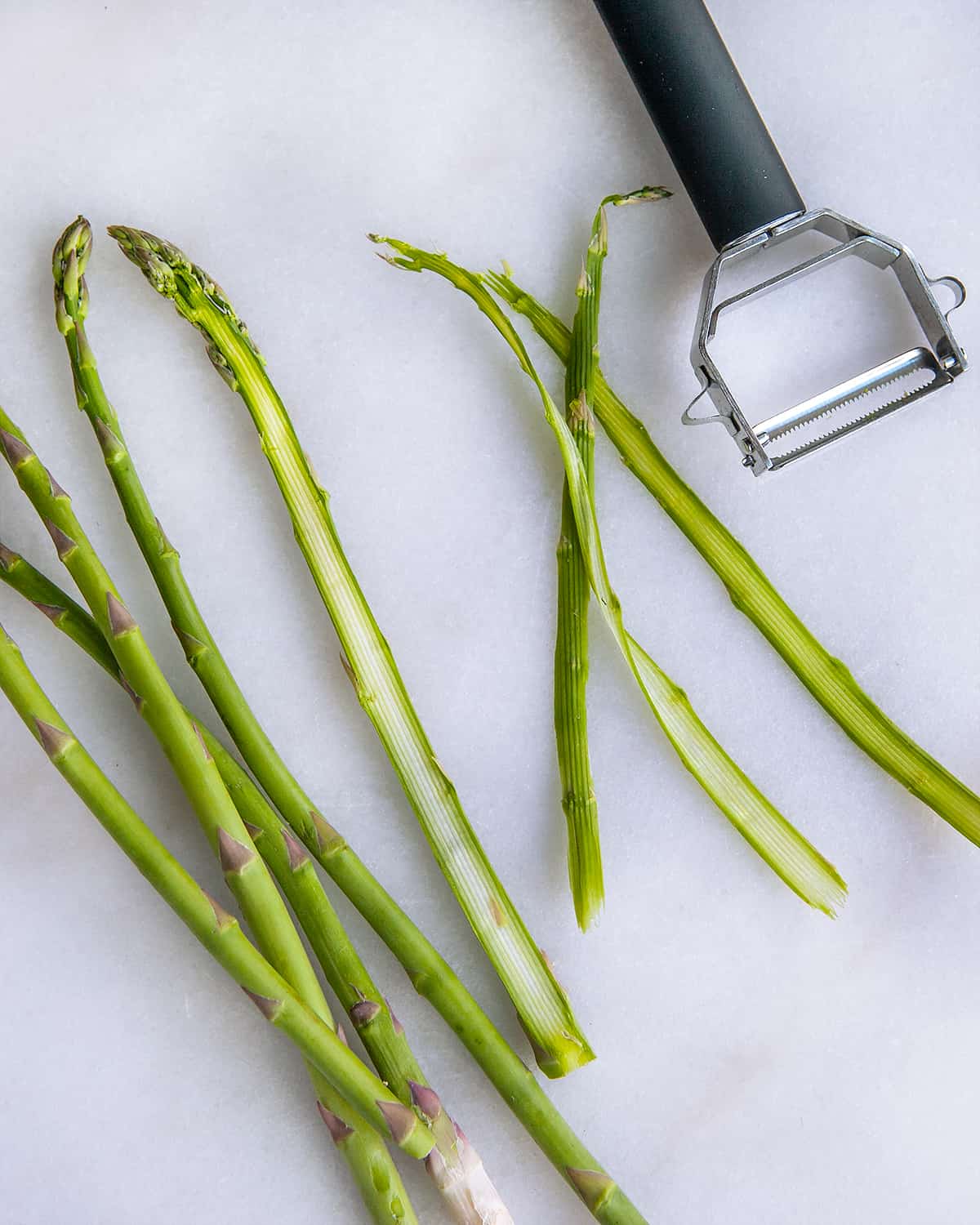 Shaving asparagus with a peeler.