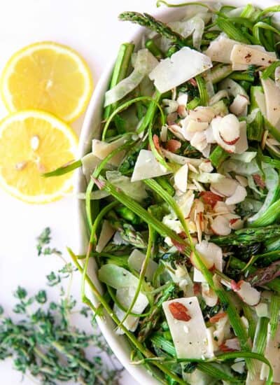 Overhead of the partial bowl of Fennel Asparagus Salad, lemon slices on the side.