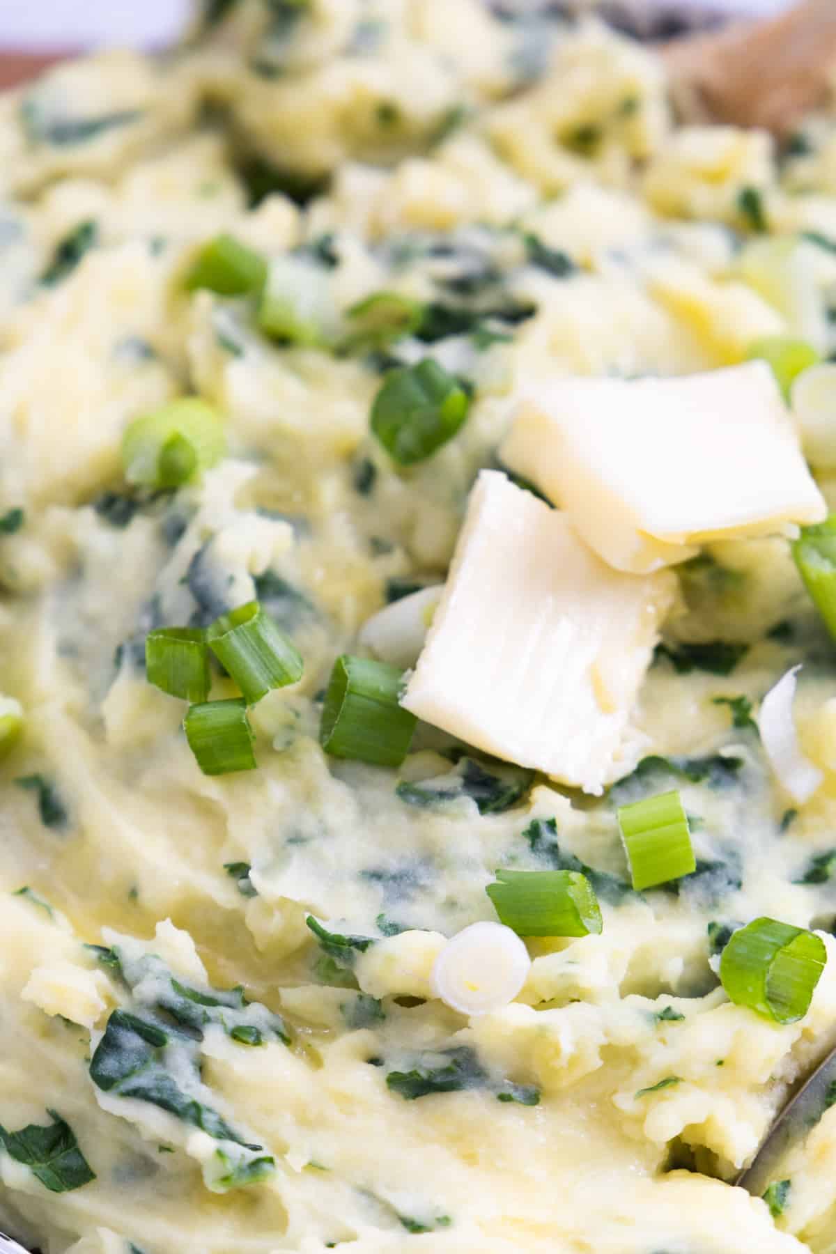 close up of 2 squares of butter on mashed potatoes with chopped greens and chopped green onions