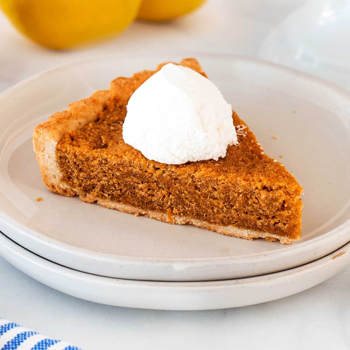 Square photo of treacle tart on a plate with whipped cream.