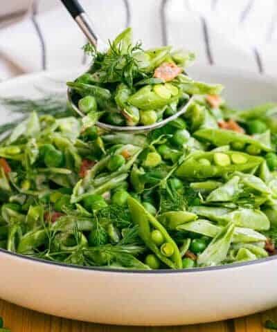Spooning out Creamy Snap Peas and Bacon from a white bowl.