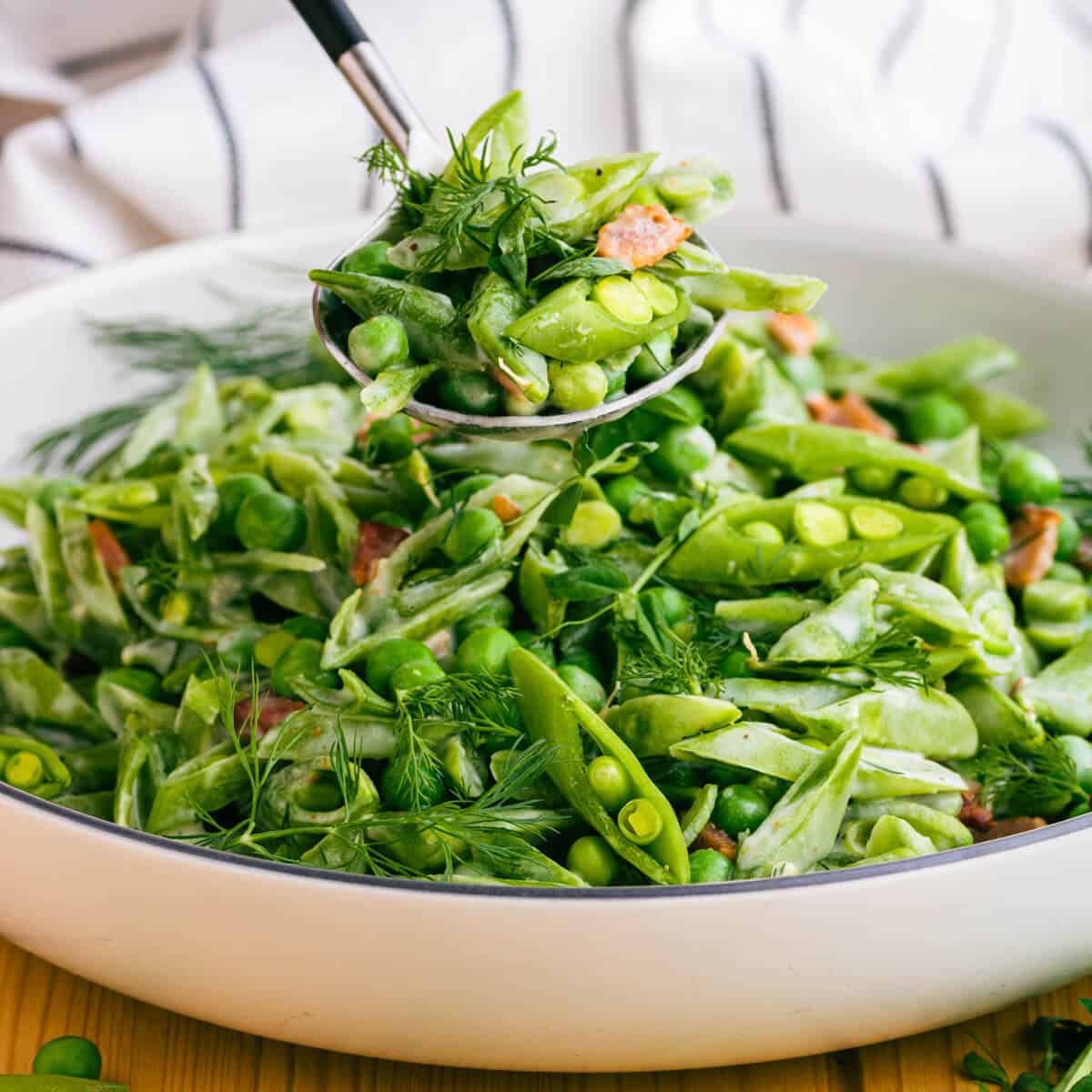 A spoonful of bright green sugar snap peas, Spring peas, and bacon with fresh green herbs in a cream sauce.