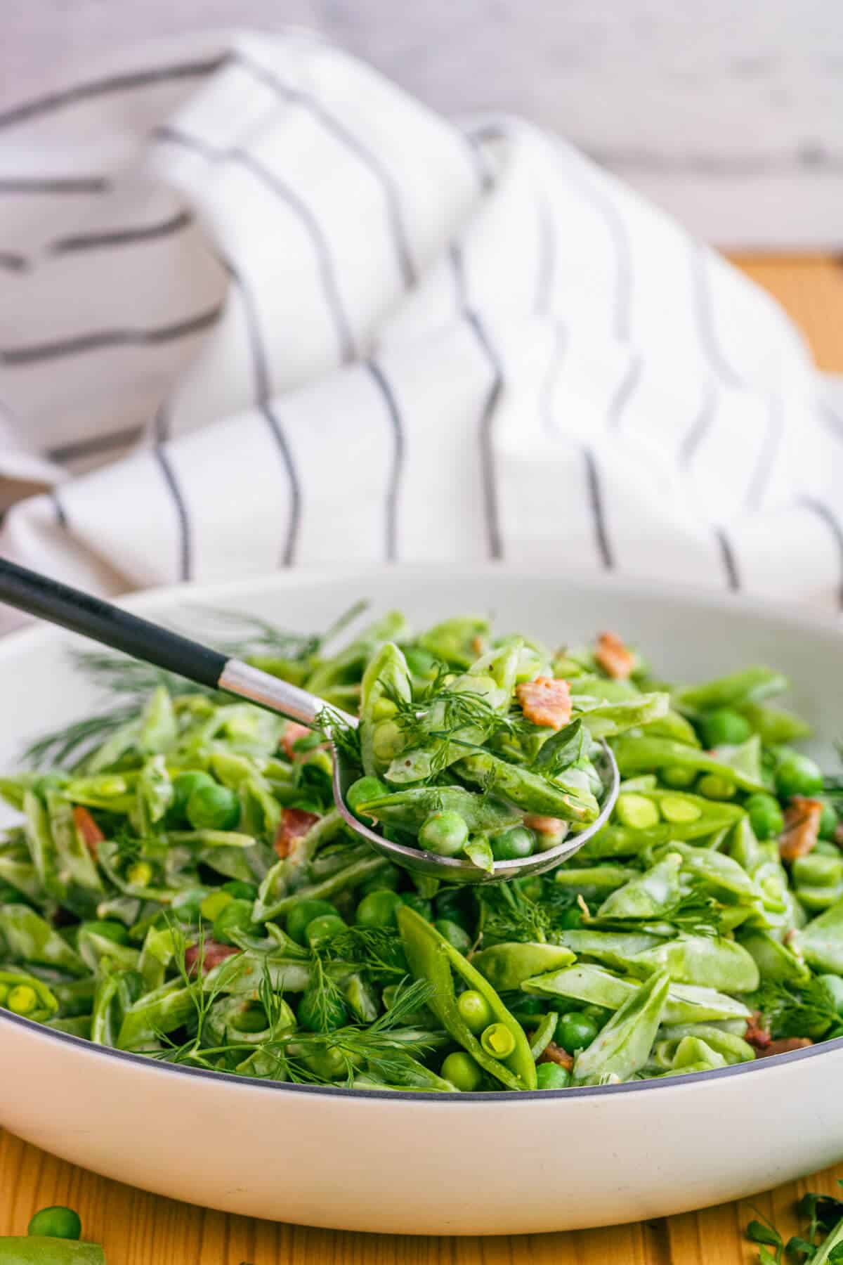 A spoonful of bright green sugar snap peas, Spring peas, and bacon with fresh green herbs in a cream sauce.