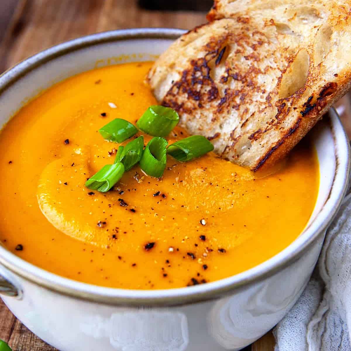 Square photo of carrot ginger soup with a slice of toasted artisan bread. 