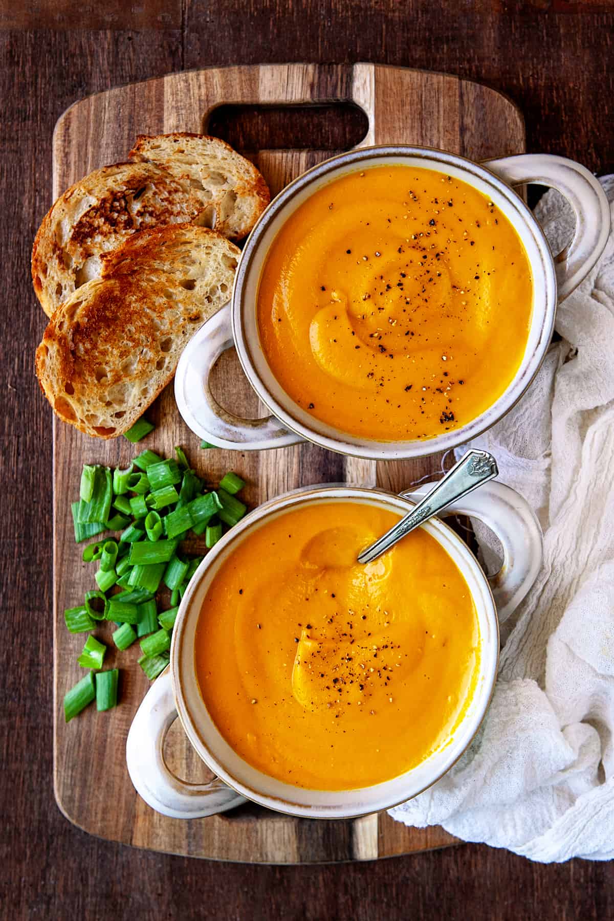 Overhead two bowls of carrot ginger soup with toasted bread. 