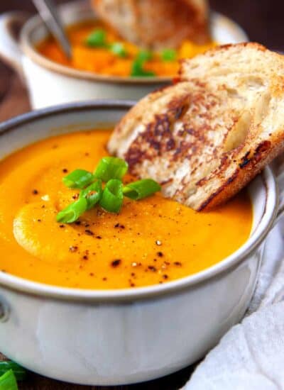 Bowl of carrot soup with green onions on top and a slice of bread.
