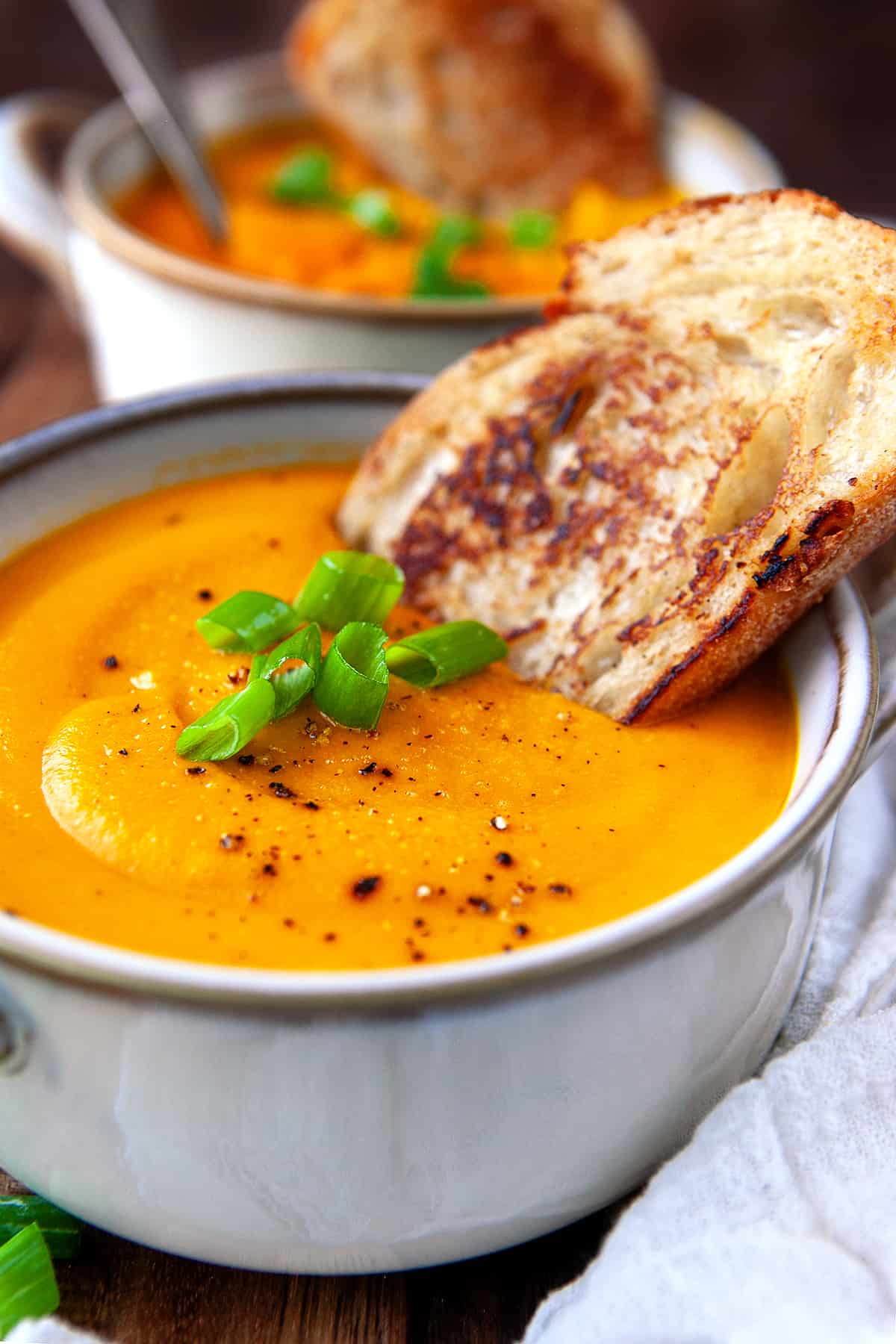 Bowl of carrot soup with green onions on top and a slice of bread. 