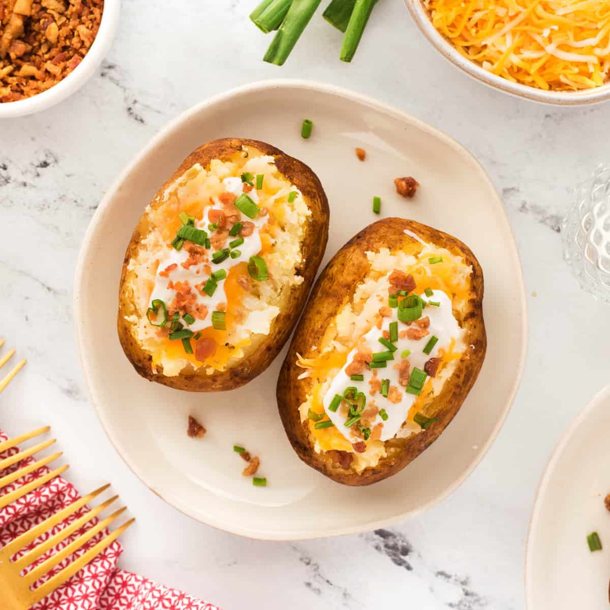 Square photo of two baked potatoes with toppings on a plate. 