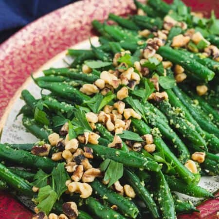 A serving platter full of vibrant Pesto Green Beans tossed with pesto and topped with chopped walnuts and fresh parsley.