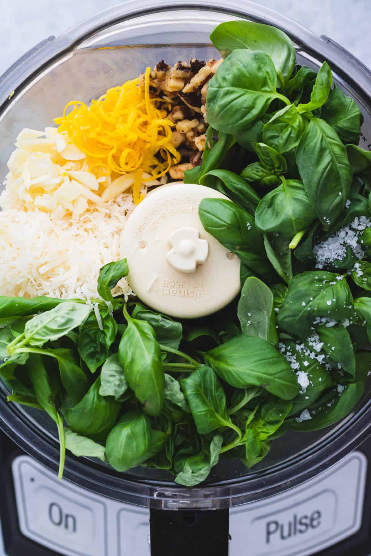 A food processor bowl full of ingredients needed to make walnut basil pesto.