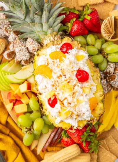 Easy fruit dip made with cool whip and pina colada flavors showcased in a halved pineapple surrounded by fresh fruit.