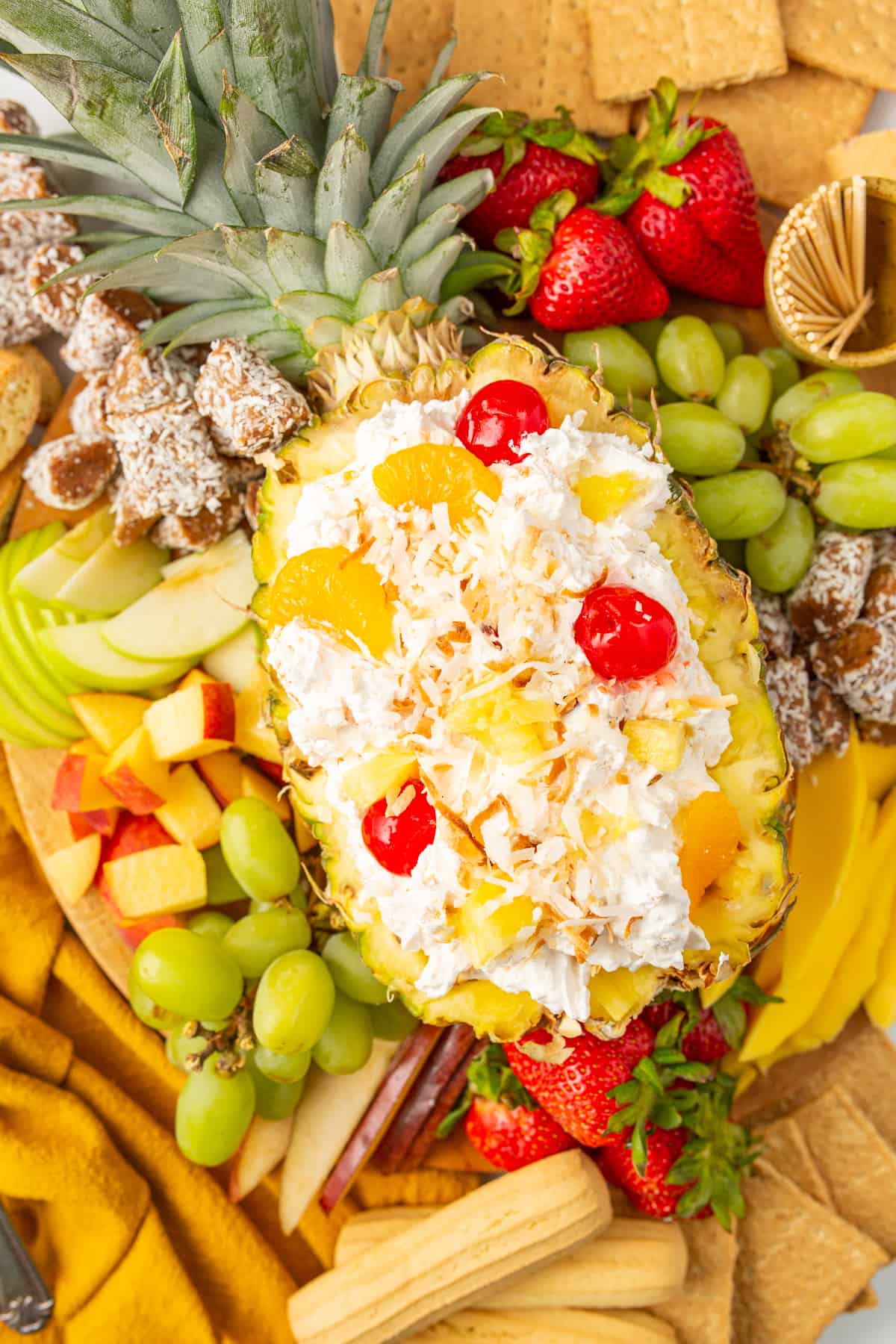 Easy fruit dip made with cool whip and pina colada flavors showcased in a halved pineapple surrounded by fresh fruit.