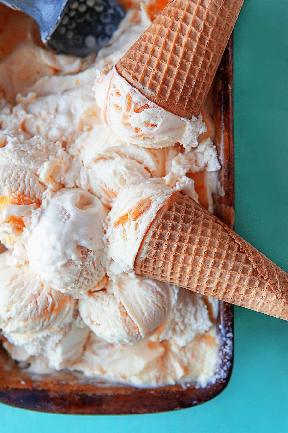Scoops of peach ice cream and cones piled in a container of ice cream. 