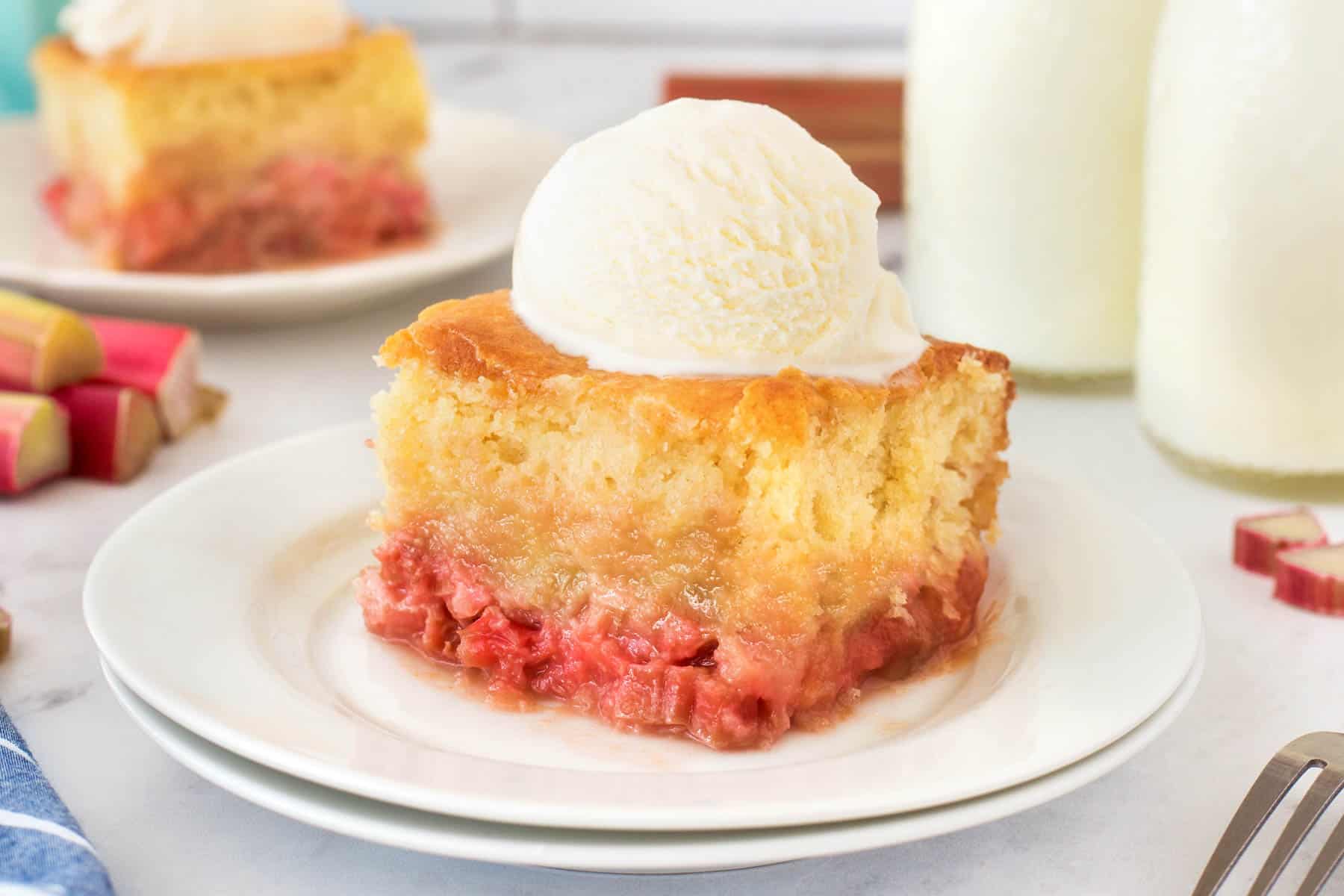 Horizontal of rhubarb pudding cake on a plate with ice cream. 
