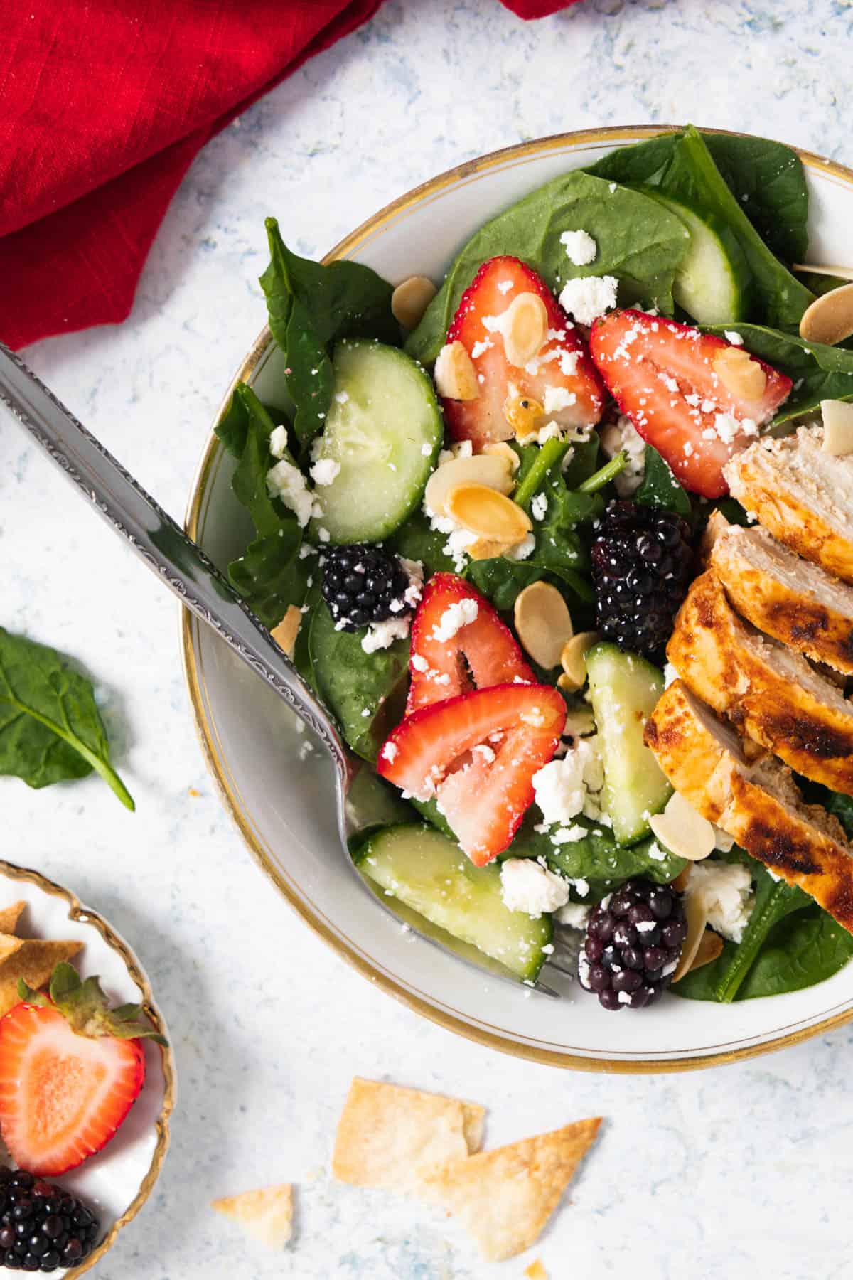 view of half a plate with spinach, strawberries, cucumber, blackberry salad with grilled chicken on top