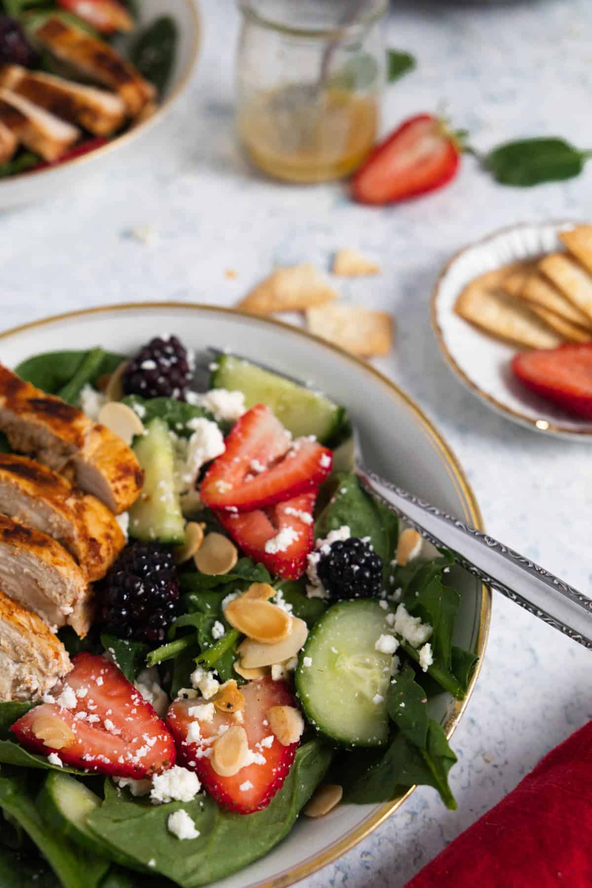 view of half a plate with spinach, strawberries, cucumber, blackberry salad with grilled chicken on top