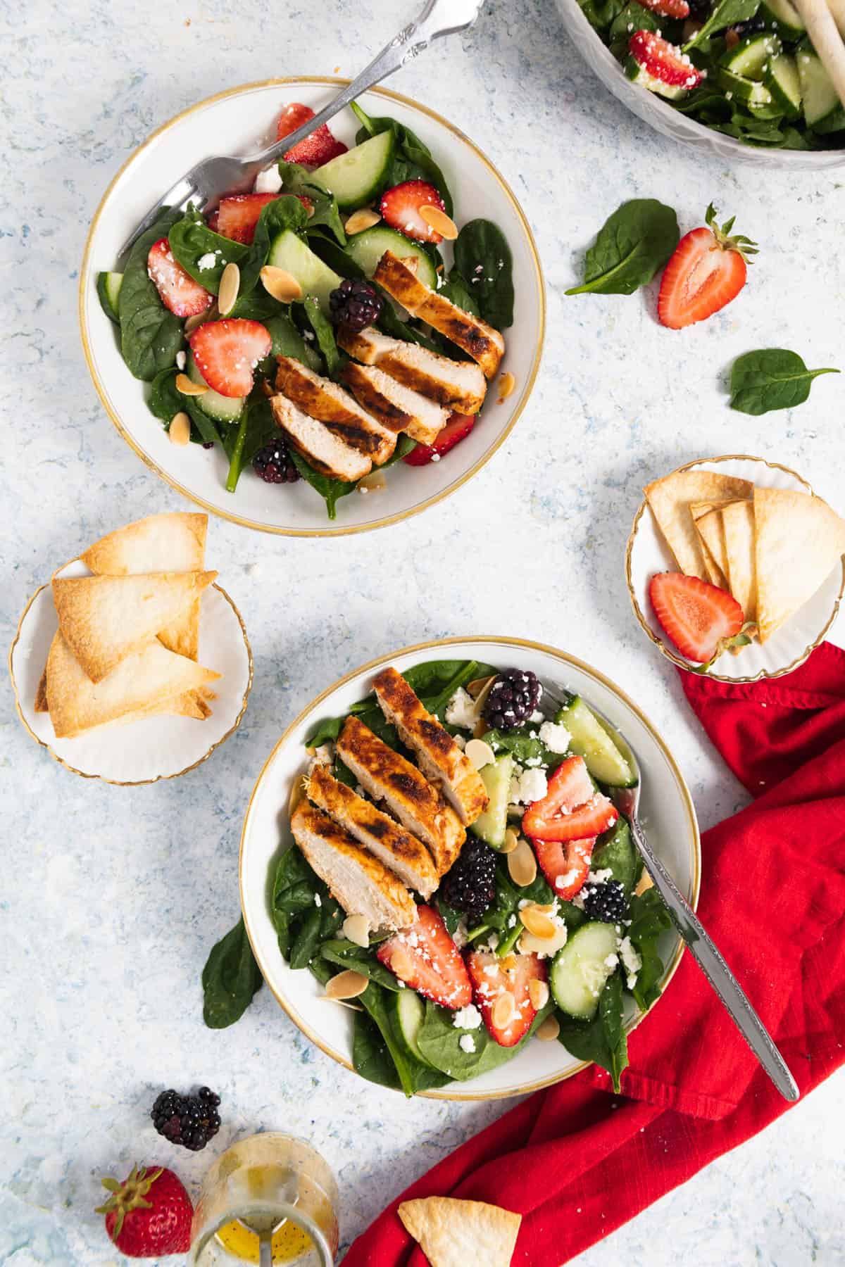 2 plates with spinach and strawberry salad with a fork in each, 2 small plates with tortilla chips on the side