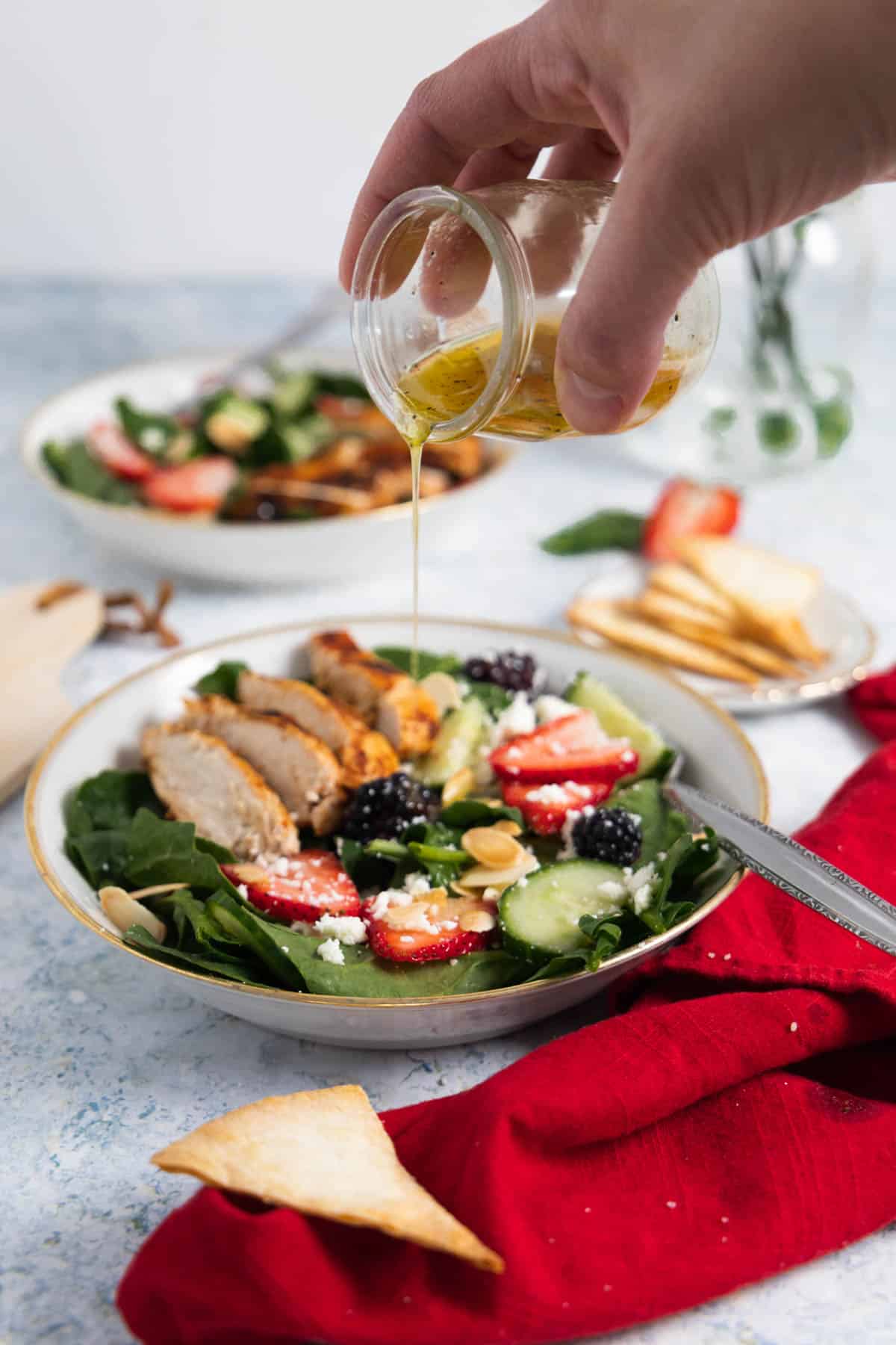 dressing being poured on a spinach salad