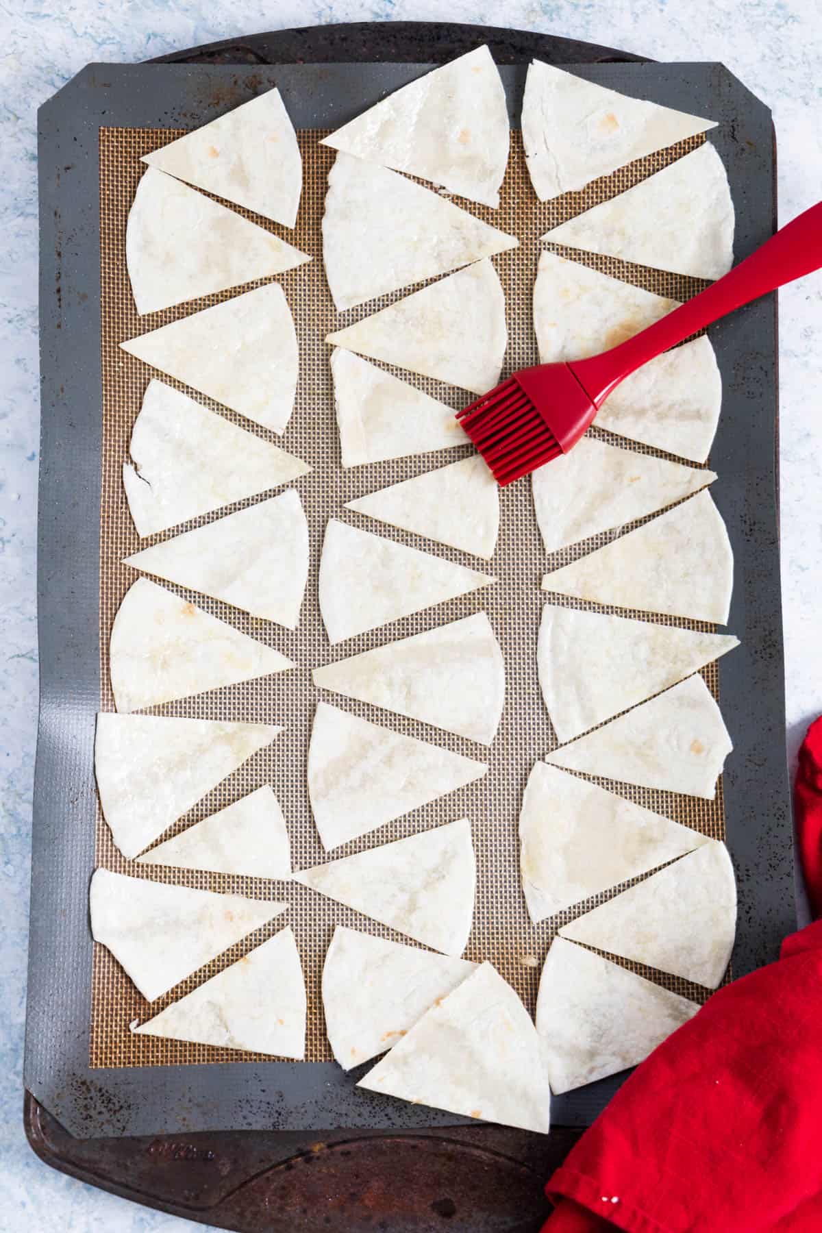 tortilla cut in triangle and lined up on a baking tray with a silicone brush on the side.