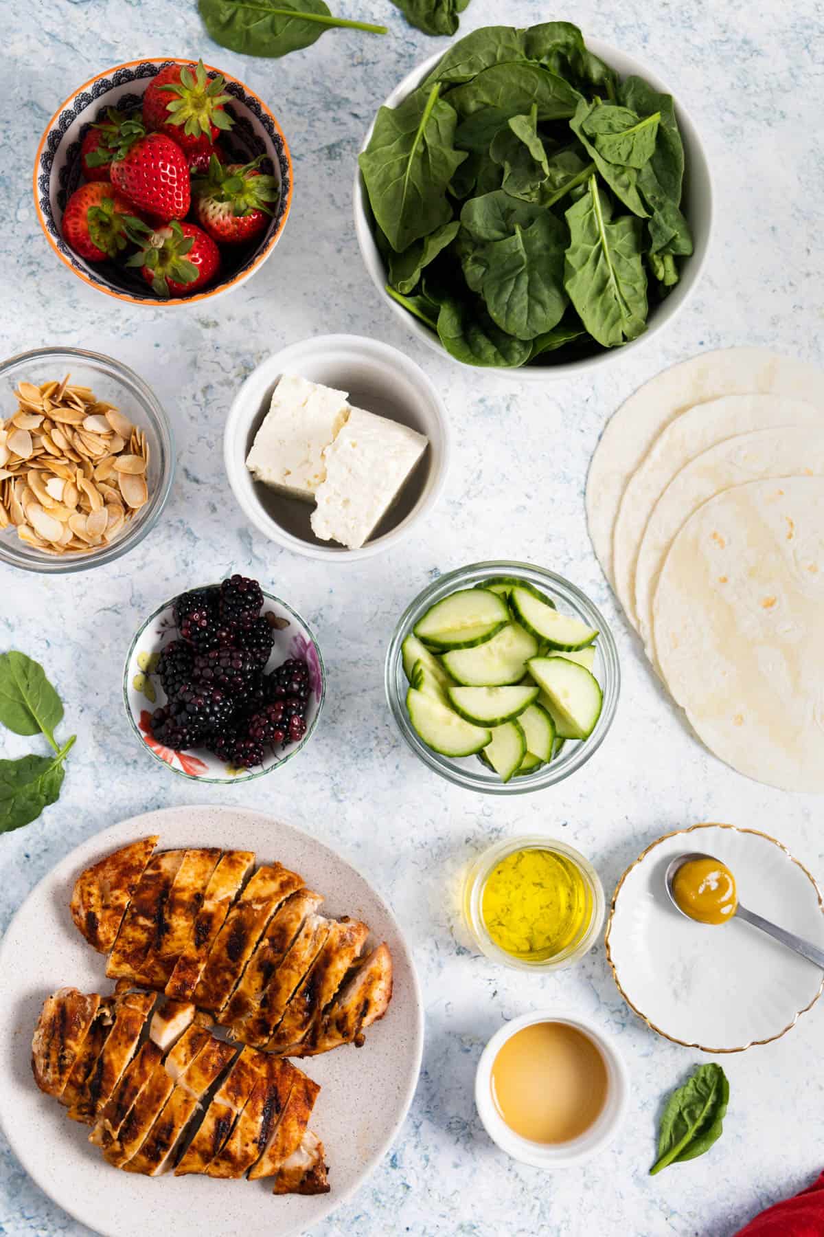 ingredients for a salad: spinach, strawberries, blackberries, cucumber, feta, toasted almond, grilled chicken, tortillas