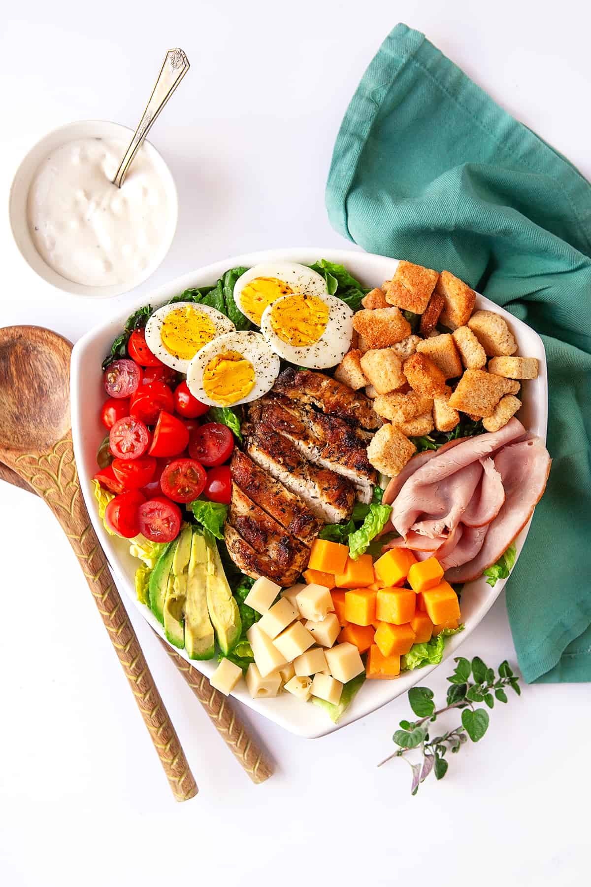 Overhead Chef Salad in a triangle bowl with salad tongs and dressing in a dish. 
