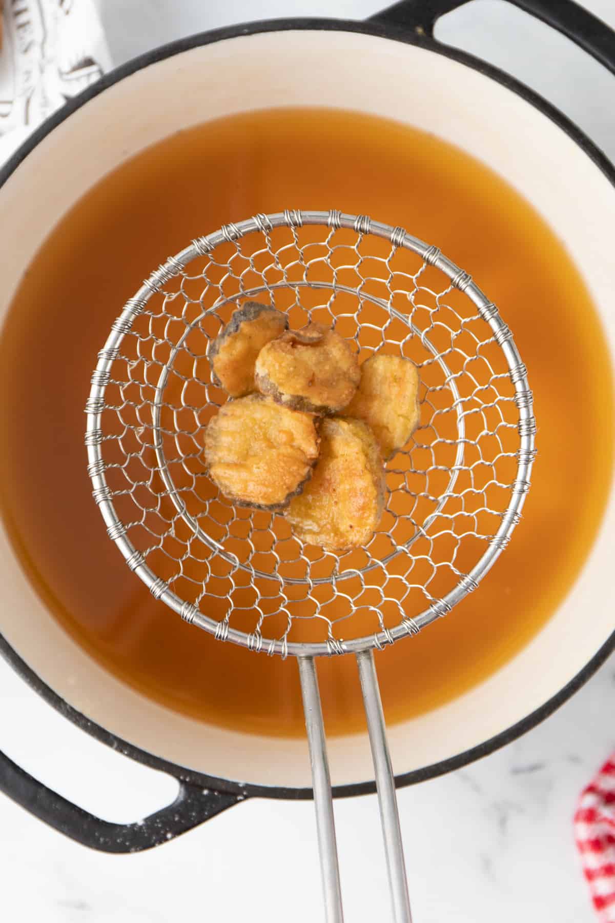 overhead image of deep fried pickles in a spider strainer over a dutch oven of hot oil