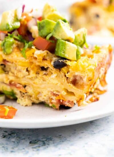 Close up of a piece of Mexican breakfast casserole with black beans and avocado and tomato on top.