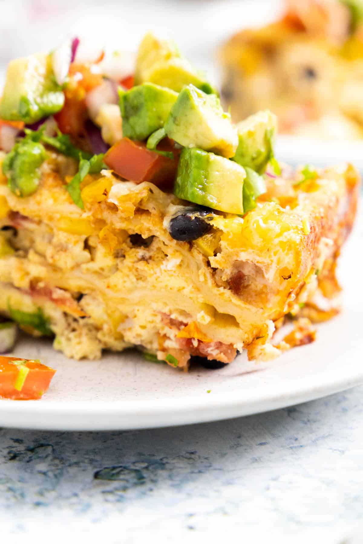 Close up of a piece of Mexican breakfast casserole with black beans and avocado and tomato on top.