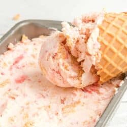A sugar cone with ice cream in a container of ice cream