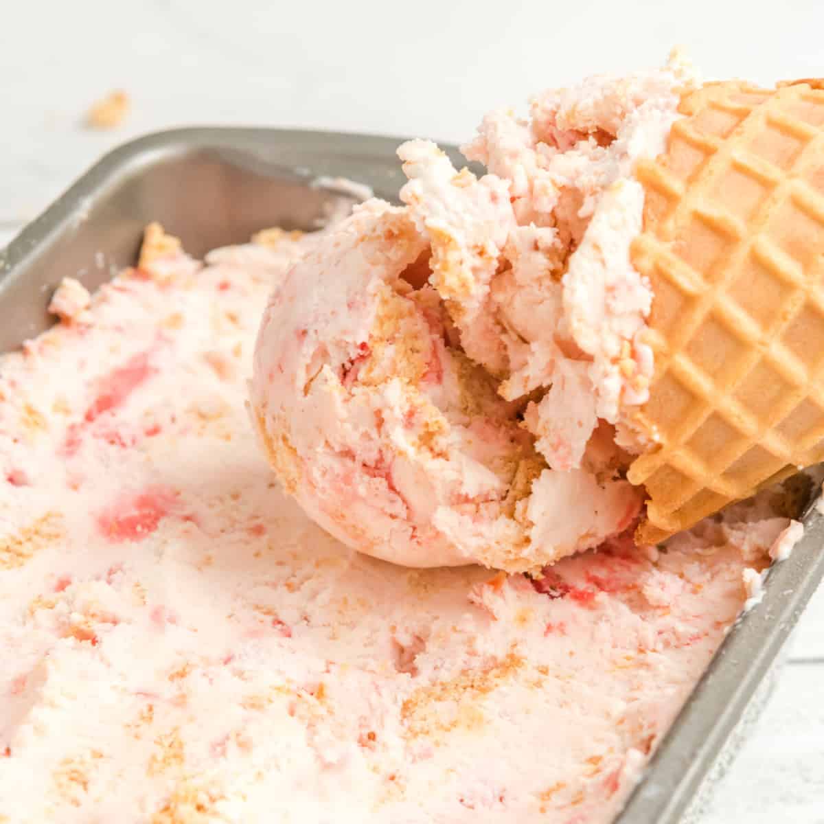 Ice cream cone laid in a container of ice cream. 