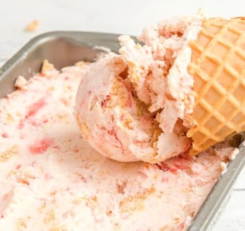 Strawberry Cheesecake Ice Cream in a cone lying in the container of ice cream.