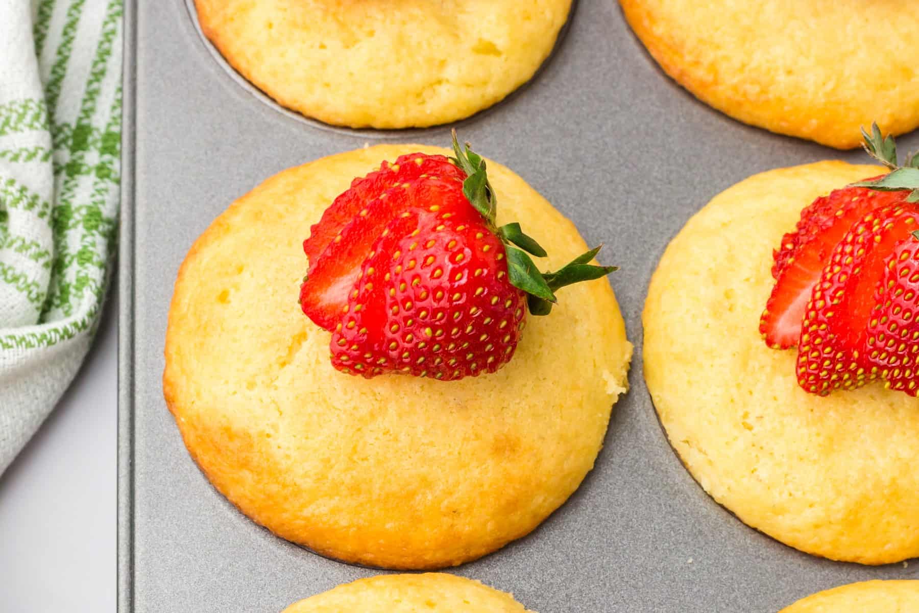 Horizontal overhead of strawberry pancake muffins with partially sliced strawberries on top. 