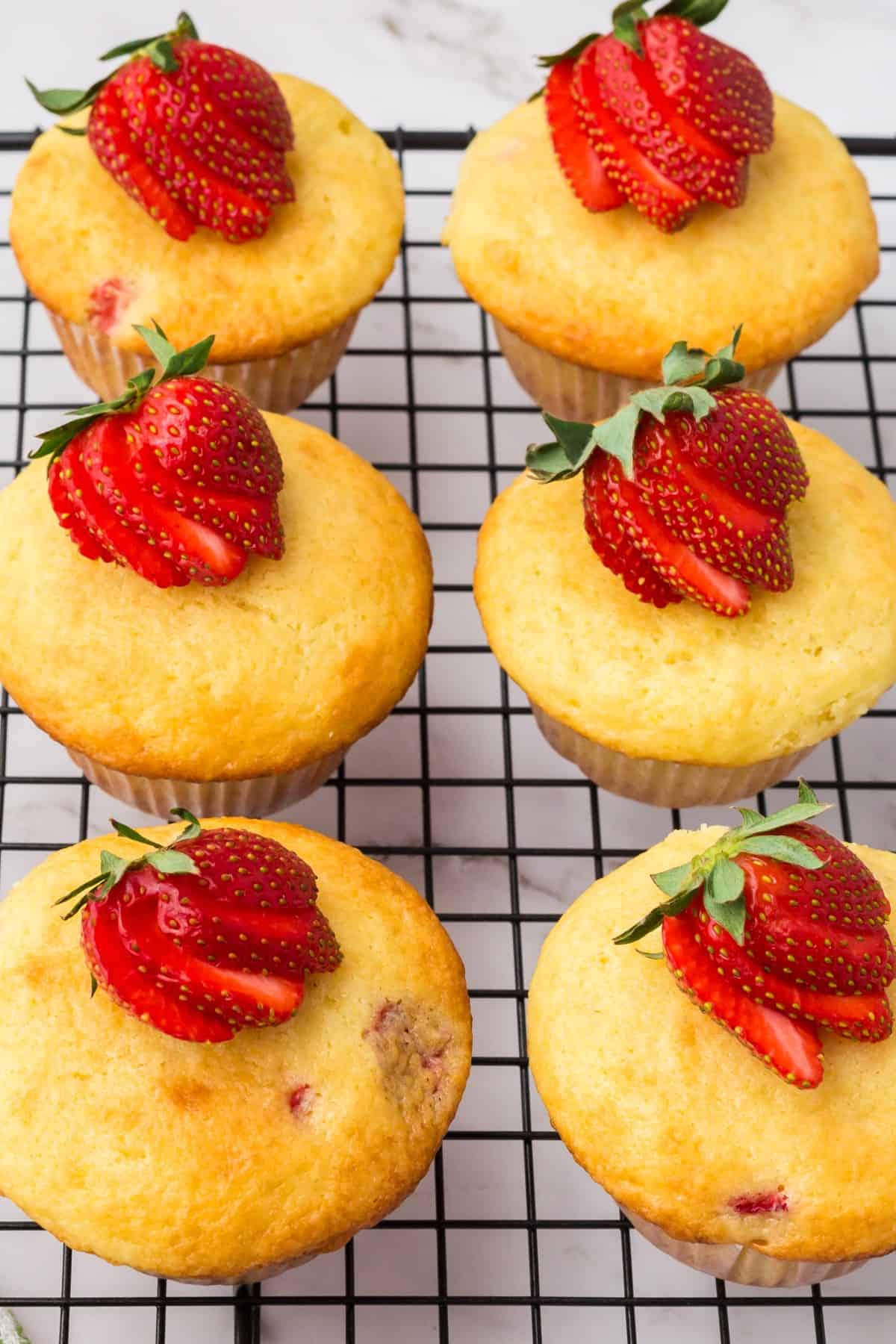 Strawberry Pancake Muffins on a cooling rack with fresh partially sliced strawberries on top. 