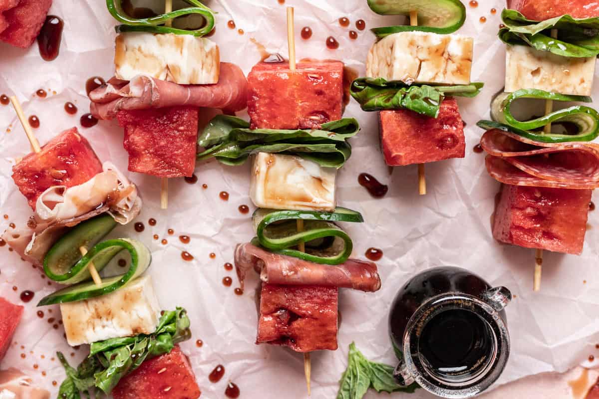 Horizontal overhead photo of watermelon feta skewers with a small container of balsamic reduction. 