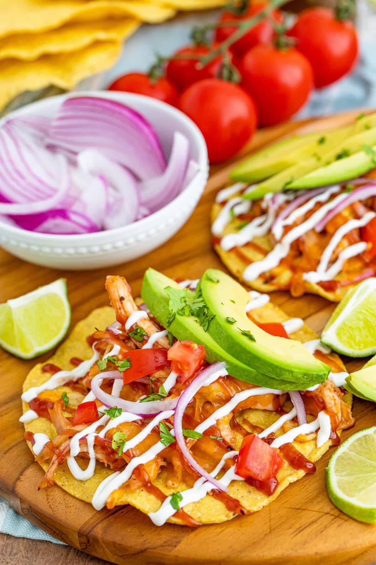 BBQ Chicken Tostadas with slices of avocado surrounded by slices of lime. 