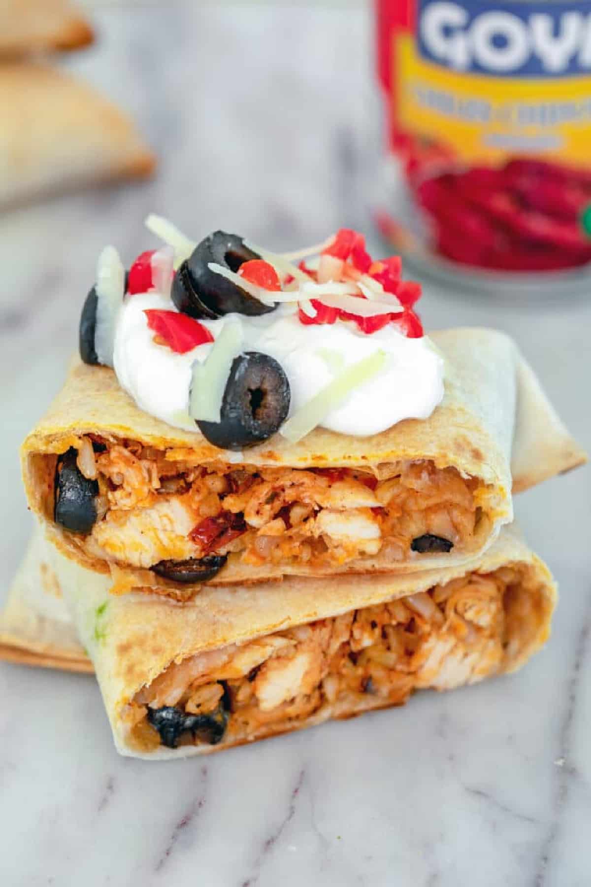 Baked chicken chimichanga cut in half and stacked with sour cream on top, olives, cheese and red pepper. 