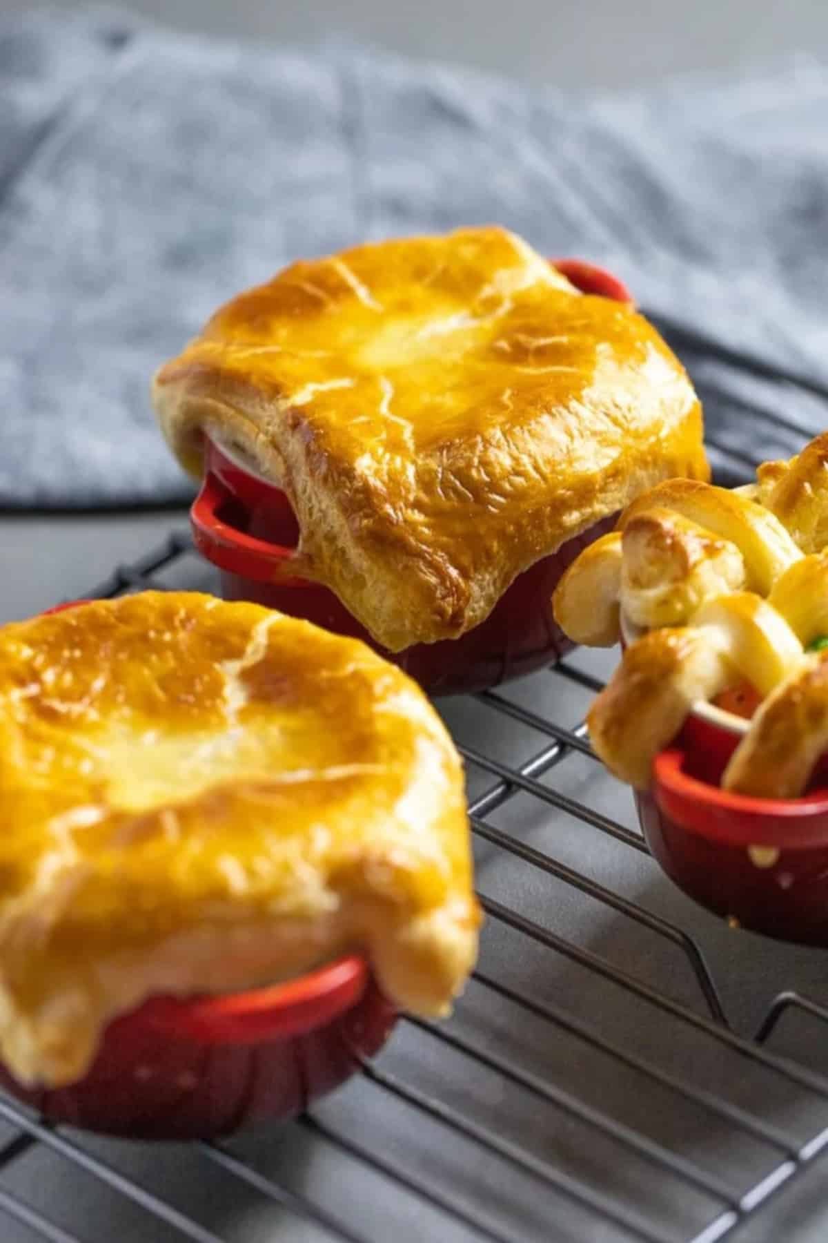 Three individual bowls of Easy Chicken Pot Pie with Puff Pastry, two with solid tops and one with a lattice top. 