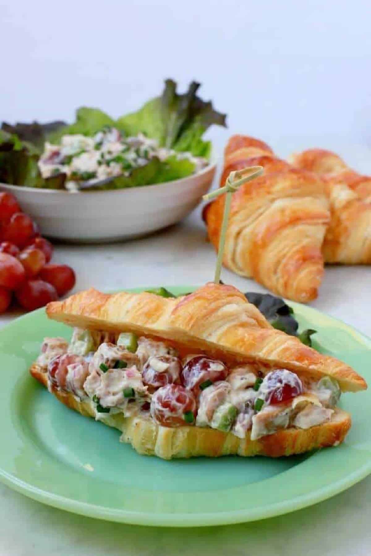 A green plate containing a croissant filled with chicken salad.