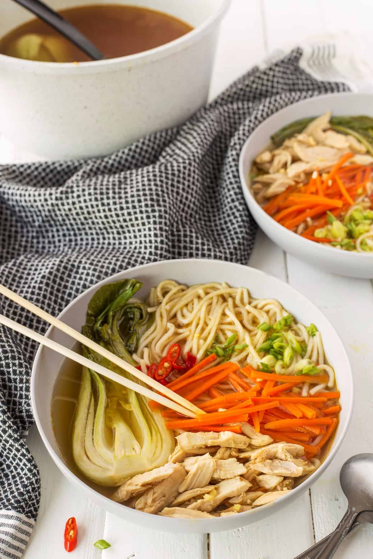 Chinese chicken noodle soup in a bowl with large piece of baby bok chok, noodles, carrots, and chicken in sections. 