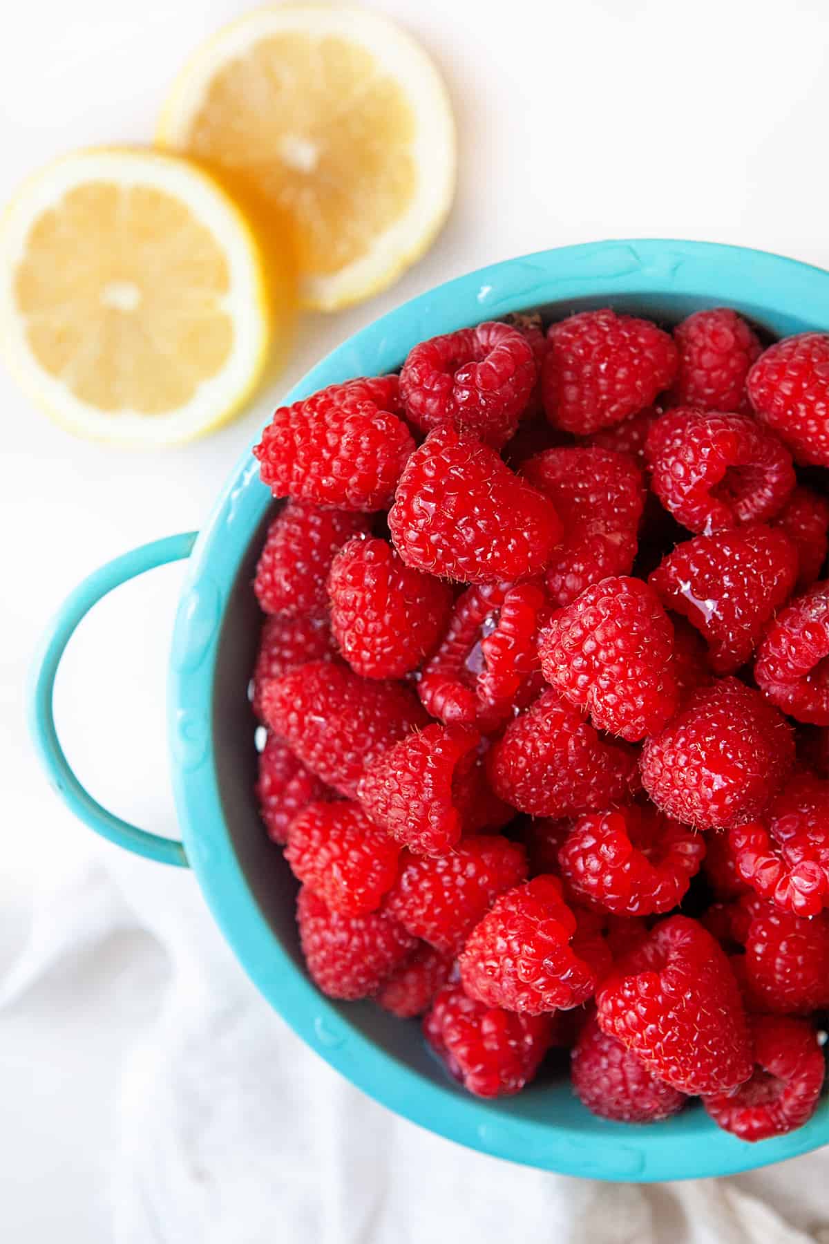Raspberries in a colander with slices of lemon on the side. 