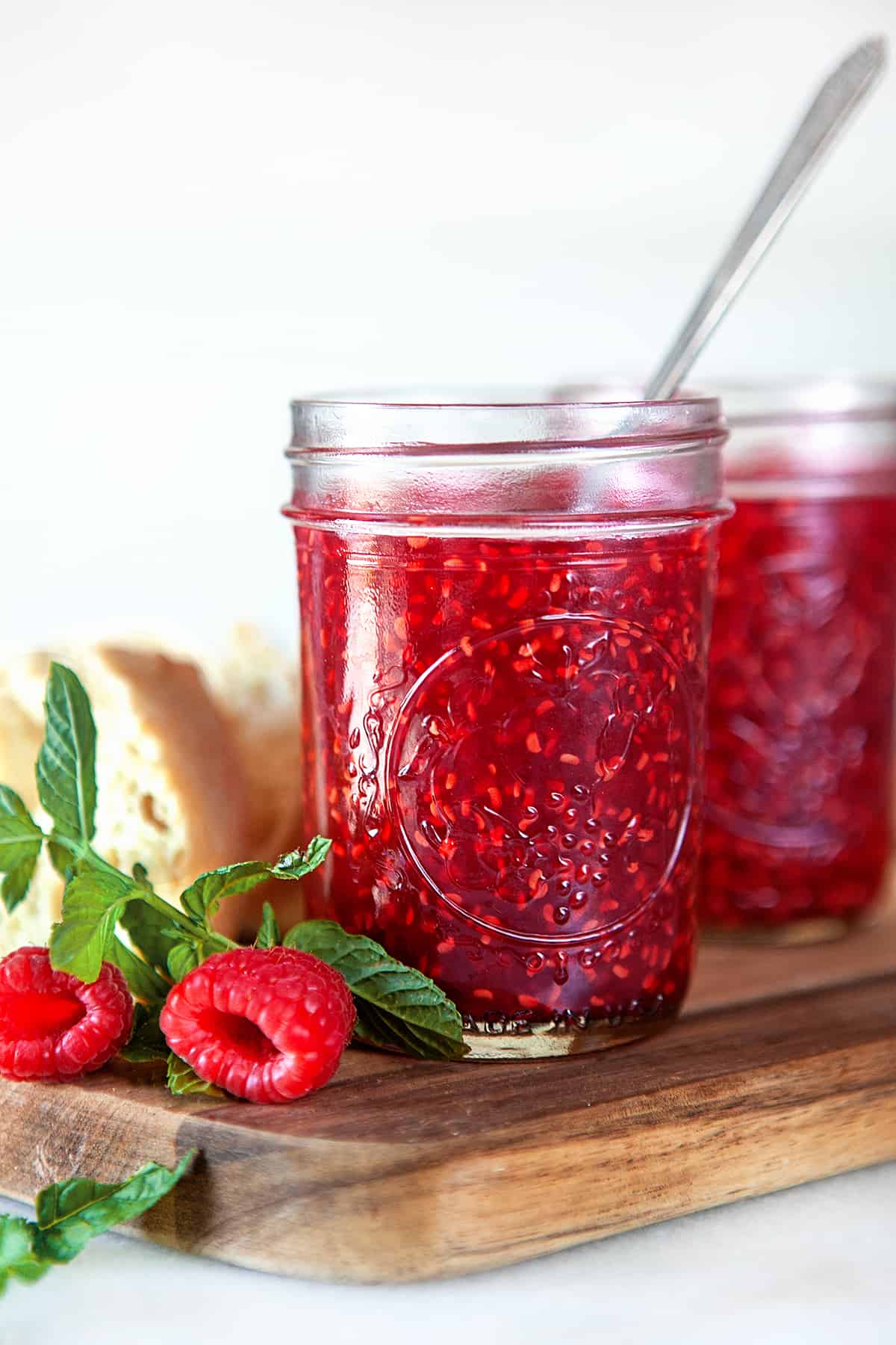 Raspberry jam in jars with a spoon in the first jar. 