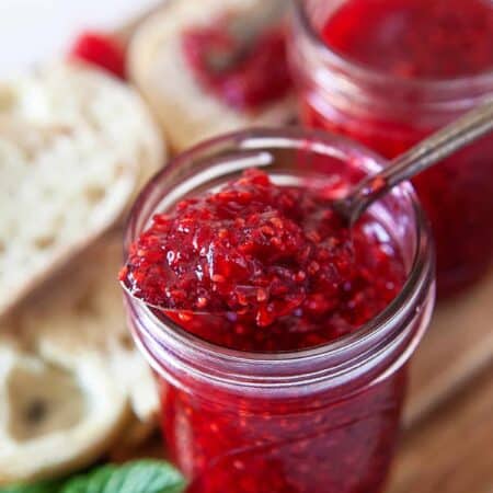 Taking a spoonful of raspberry jam from a jar.