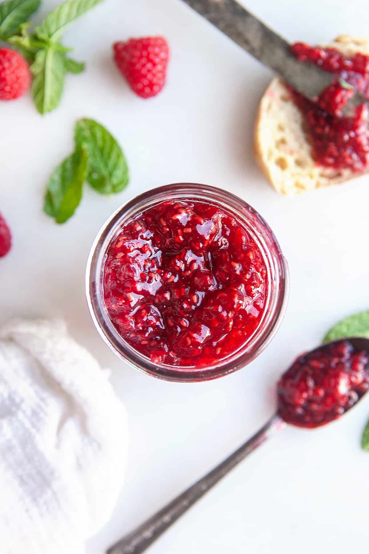 Overhead shot of raspberry jam in a jar with a spoon of jam on the side. 