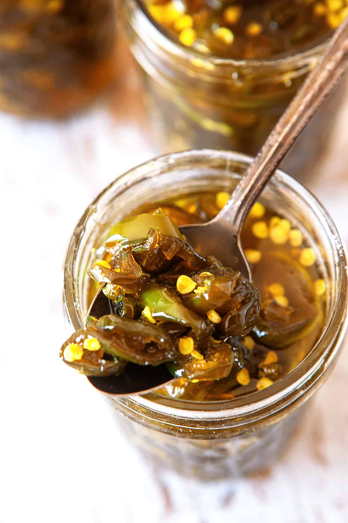 Overhead of a spoonful of candied jalapenos from a jar. 