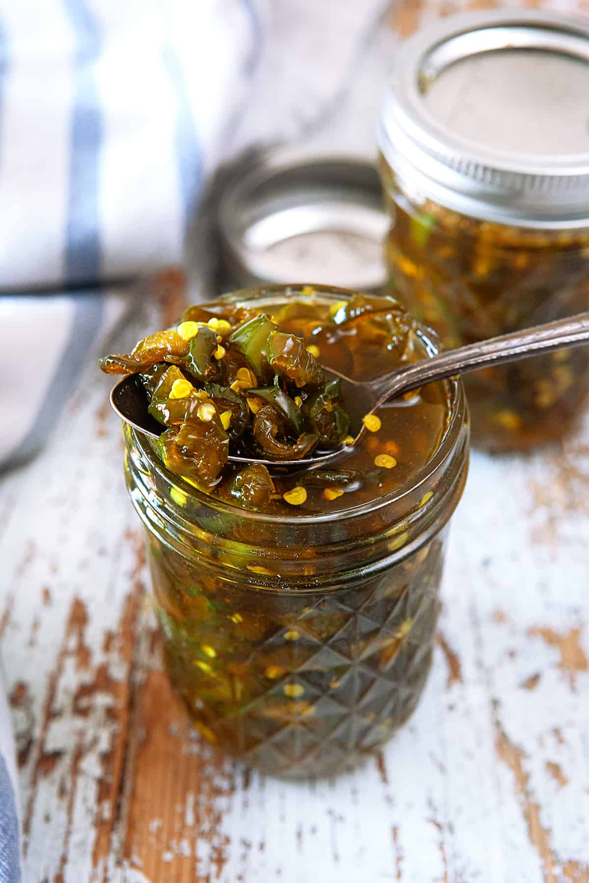 Taking a spoonful of candied jalapenos from a jar. 