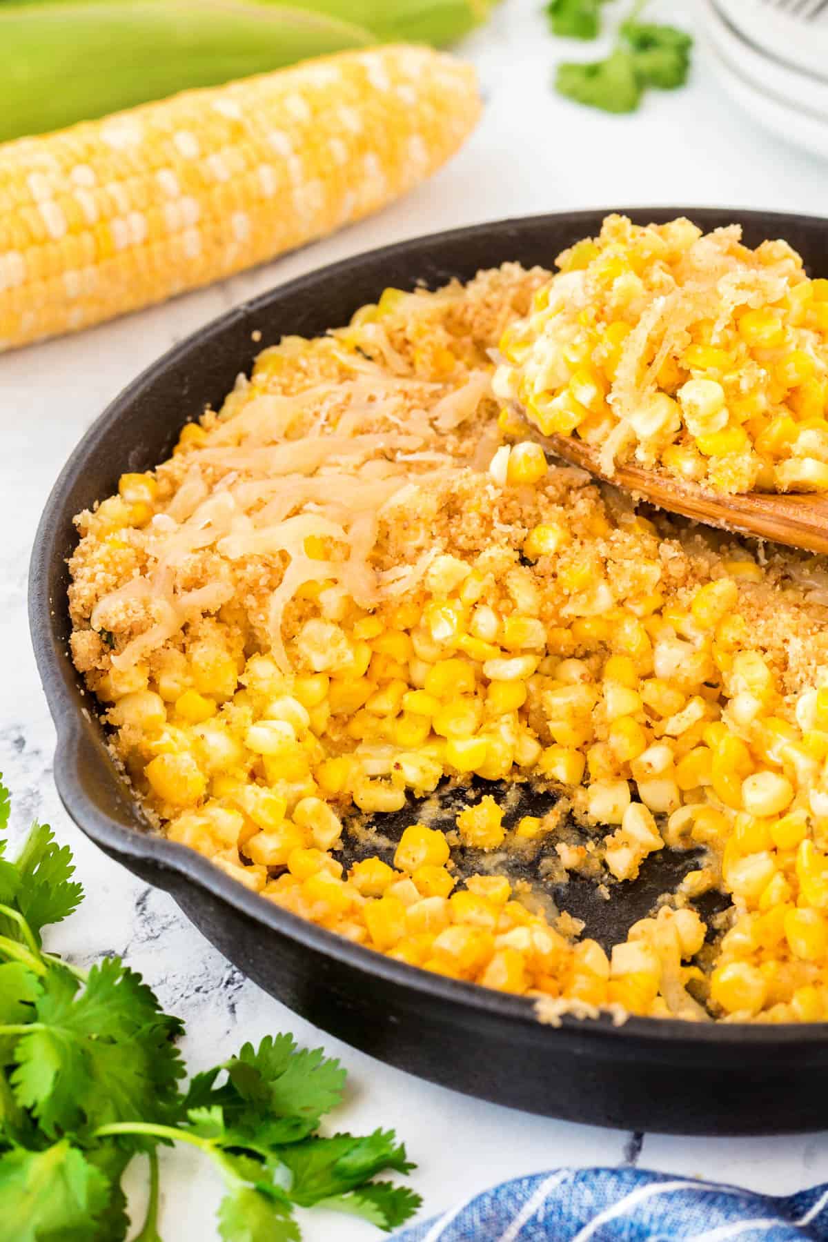 Easy Cheesy Skillet Corn in a cast iron pan with a scoop taken and resting on top. 